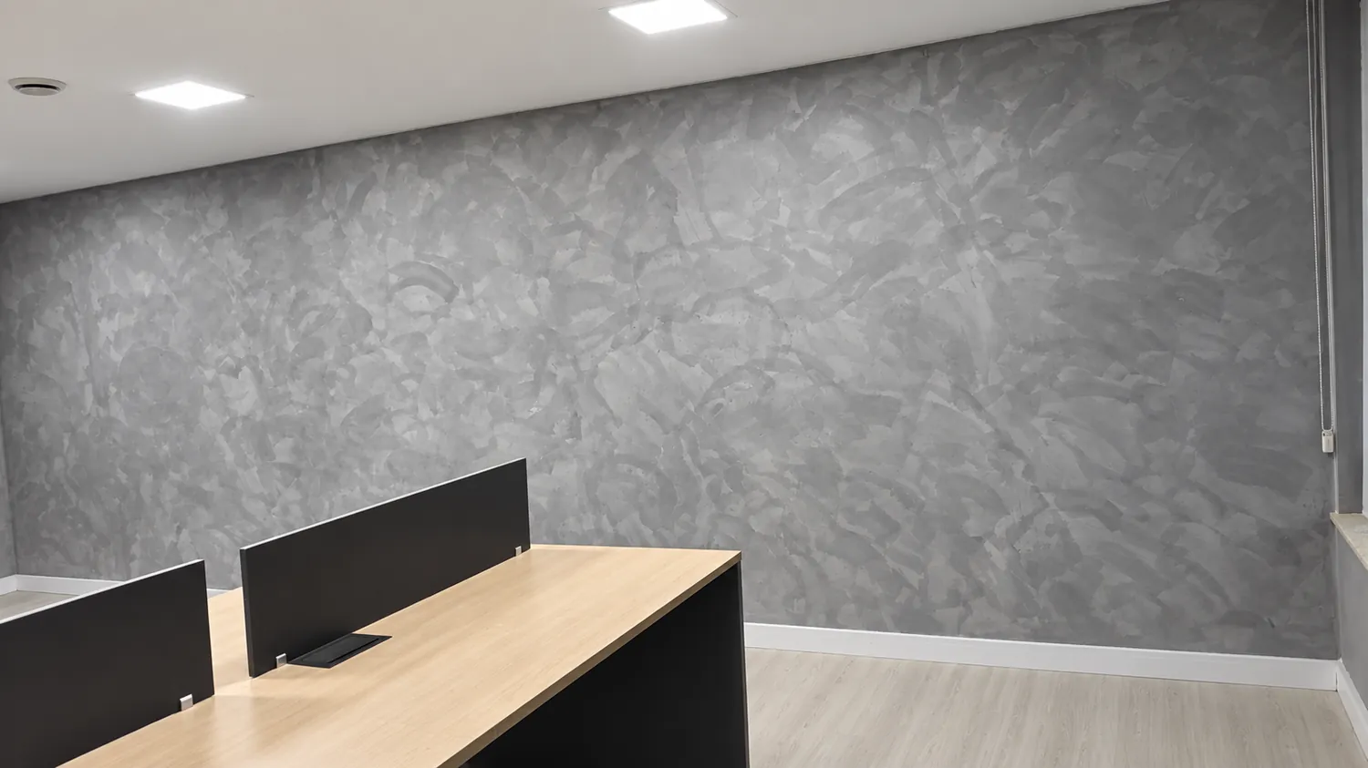 Sala comercial com parede inteira em cimento queimado cinza e estações de trabalho